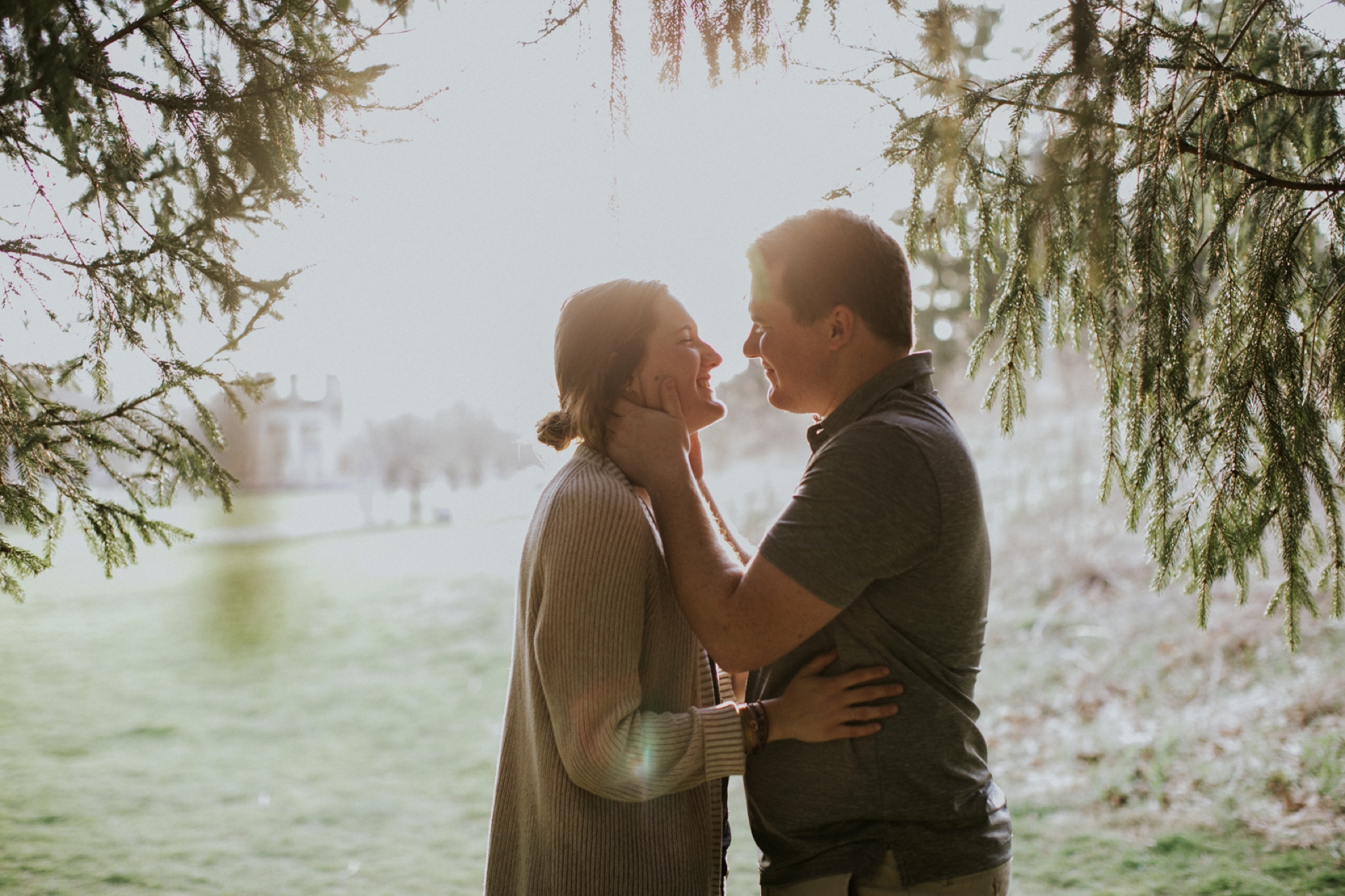 couple about to kiss under a pine tree with the sun behind them causing a beautiful glowing effect