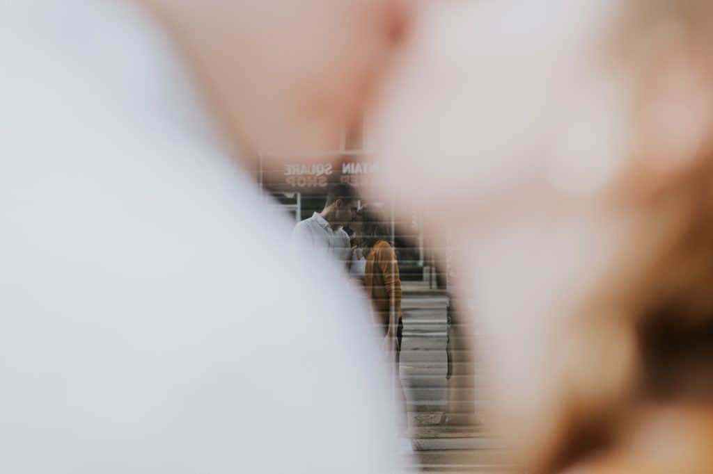 reflection of a man and woman kissing in a window during their Fountain Square Engagement
