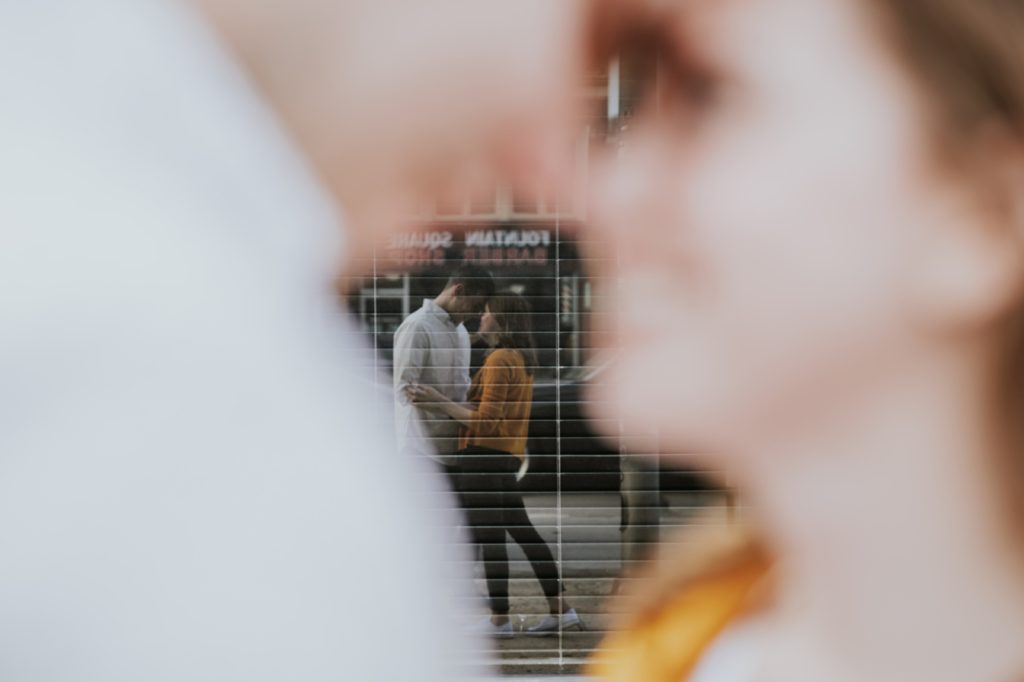 Reflection of a man and a woman in a shop window during their Fountain Square Engagement, one of the Best Indianapolis Engagement Photo Locations