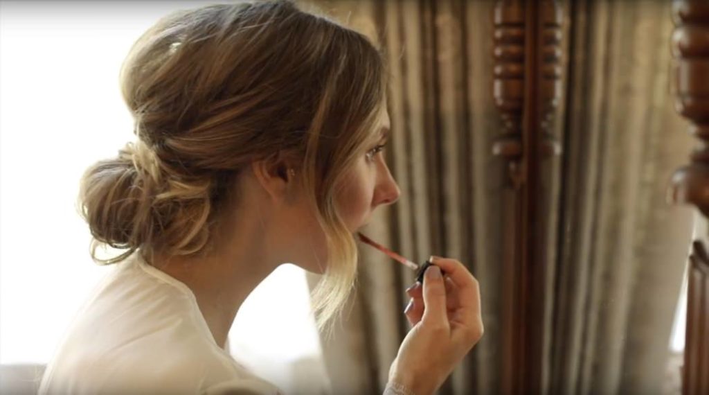 blonde women leans toward mirror while applying makeup in this benton house wedding film