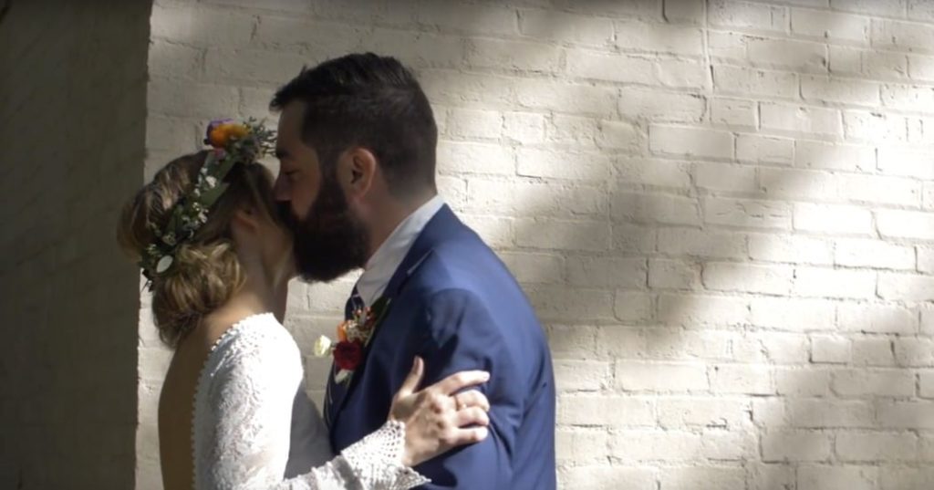 man and woman kiss in front of white brick wall in this benton house wedding film