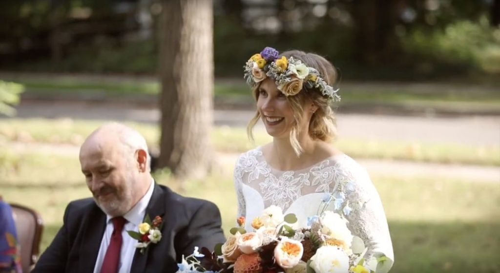 bride in floral crown brought down aisle by her father in a wheelchair