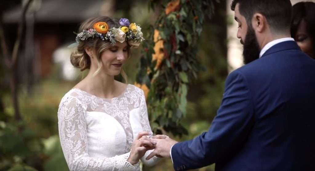 bride in floral crown slide ring onto groom's finger