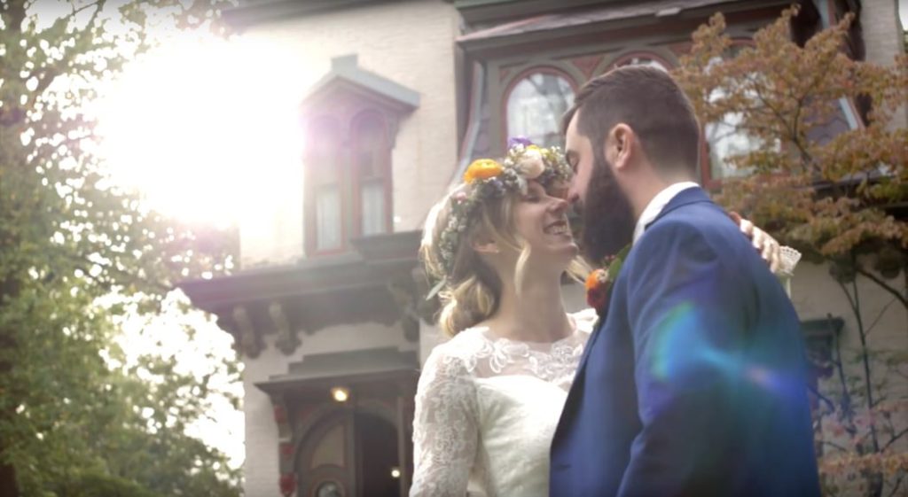 setting sun backlights bride and groom kissing in front of benton house during their wedding film