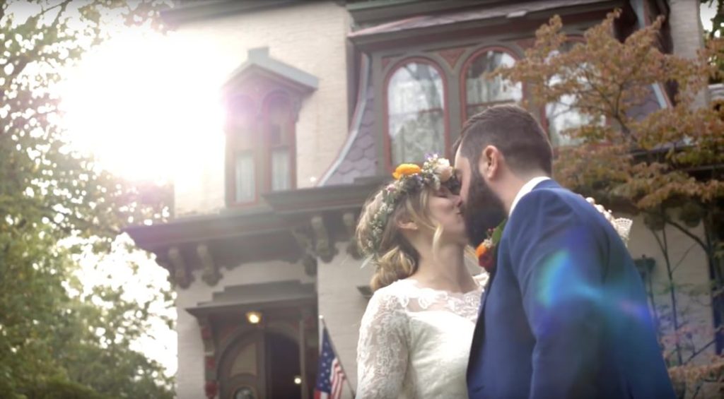bride in floral crown kisses groom in blue suit in front of benton house during their wedding film