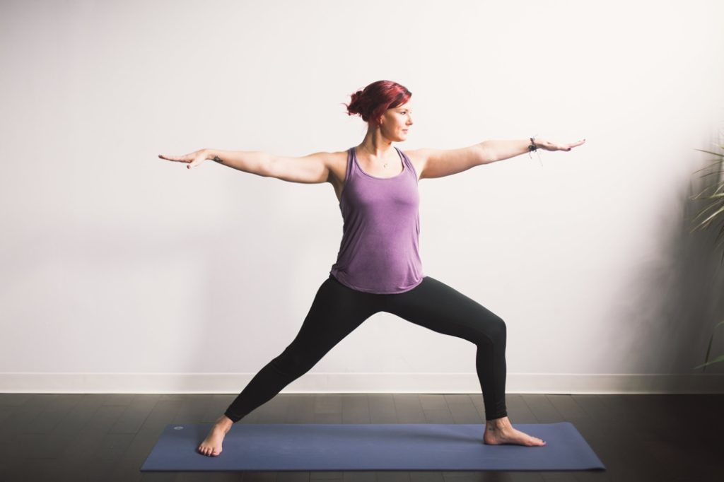 red haired woman doing warrior stance in front of a white wall during an Indianapolis Yoga Photography shoot