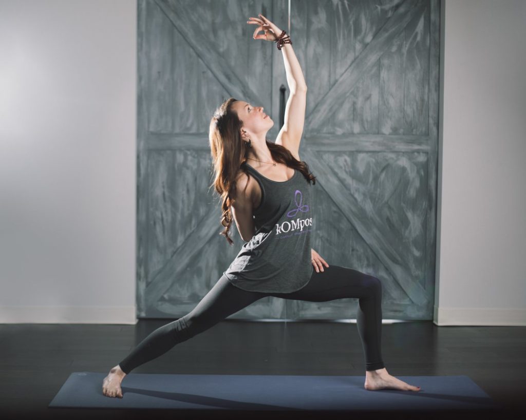 woman does a lunge with one hand over head in front of wooden doors during an Indianapolis Yoga Photography shoot