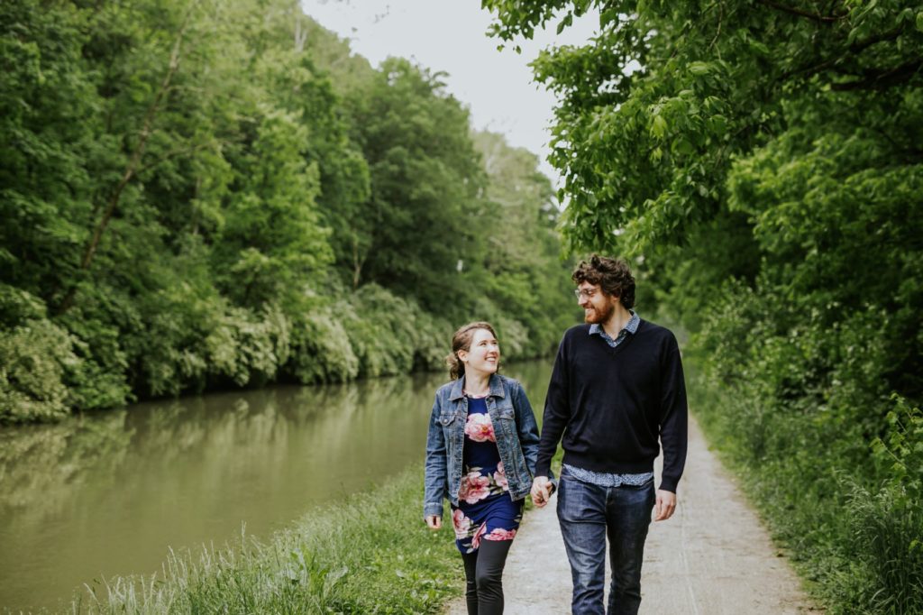 man and woman walk holding hands next to canal at their Holcomb Gardens engagement shoot