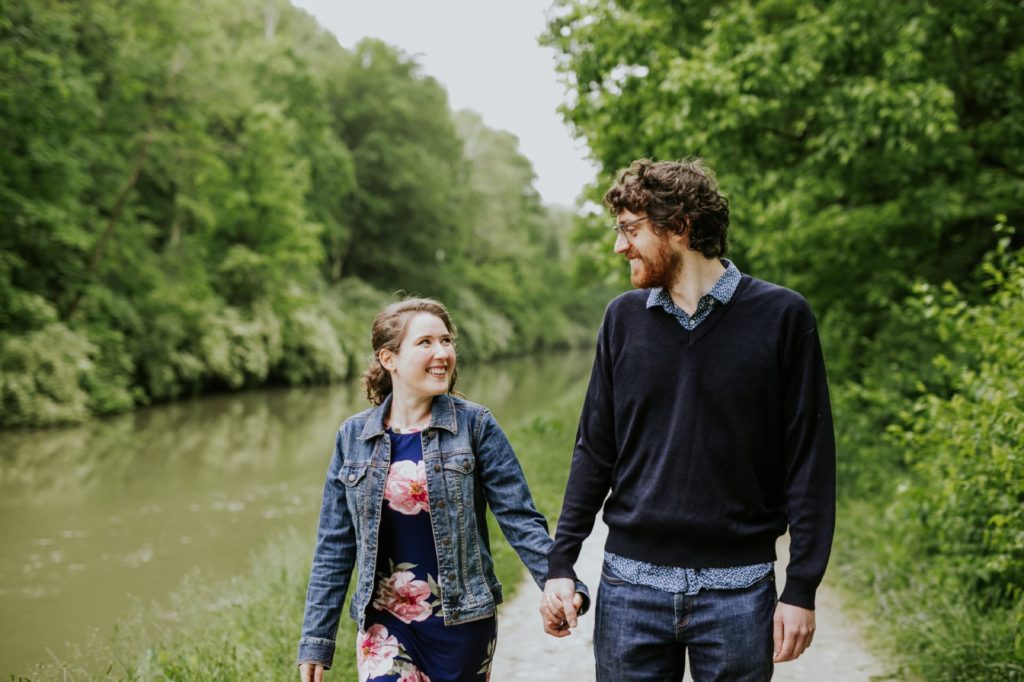 man and woman walk holding hands and smiling next to canal at their Holcomb Gardens engagement shoot
