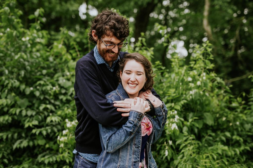 denim clad man and woman hug in front of leaves at their Holcomb Gardens engagement shoot