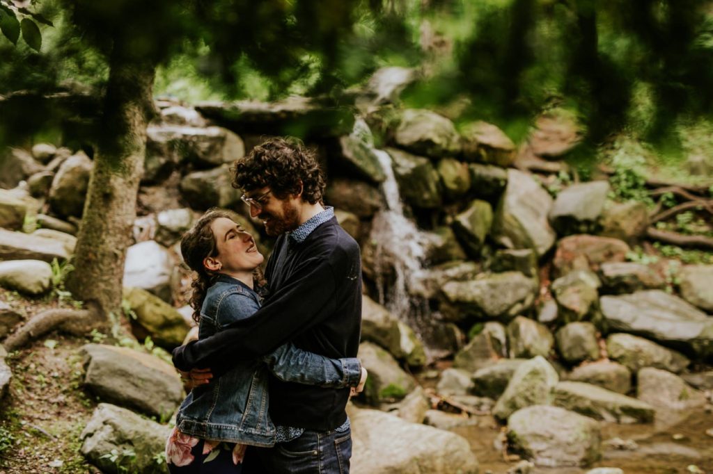 dark and moody photo of man and woman hugging and kissing in front of a waterfall at butler university