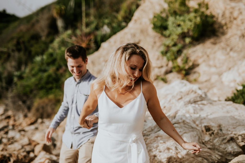 blonde woman leads man by the hand during laguna beach engagement shoot