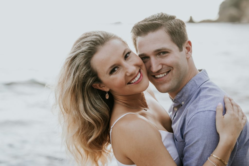 man and woman smile in front of pacific ocean during their laguna beach engagement shoot