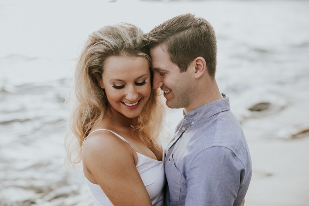 man and woman cuddle in front of pacific ocean during their laguna beach engagement shoot