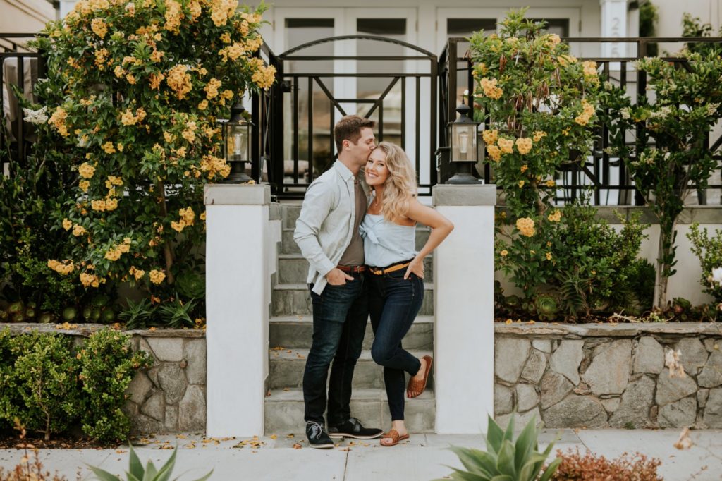 man and woman kiss and hug in entryway to a laguna beach home during engagment shoot