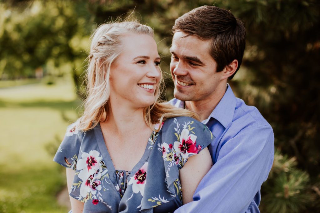 man hugs woman from behind while they both smile during their Ball State Engagement, one of the Best Indianapolis Engagement Photo Locations