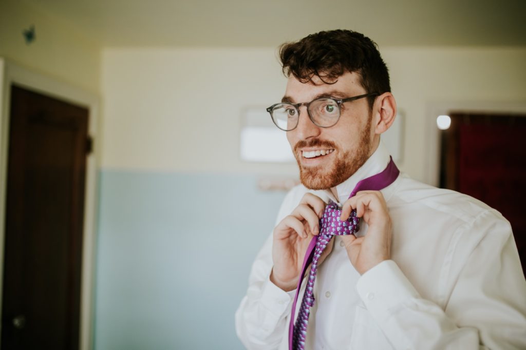 groom with glasses ties purple tie before his indy wedding