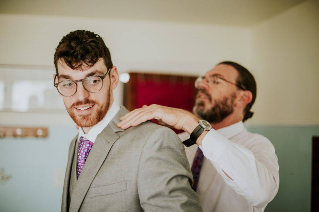 groom's dad helps groom put on suit before indianapolis wedding