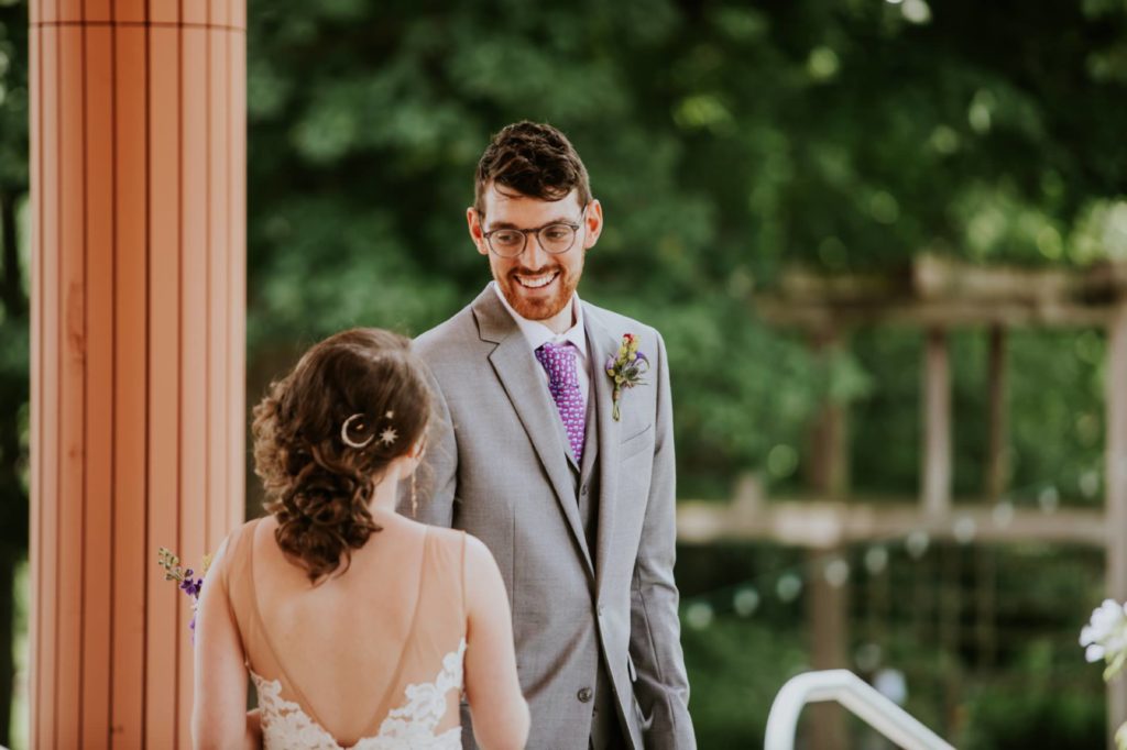 groom sees bride for first time at Indianapolis Art Center before their indiana landmarks wedding and smiles