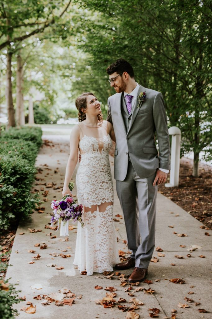 bride and groom walk down sidewalk under trees at Indianapolis Art Center