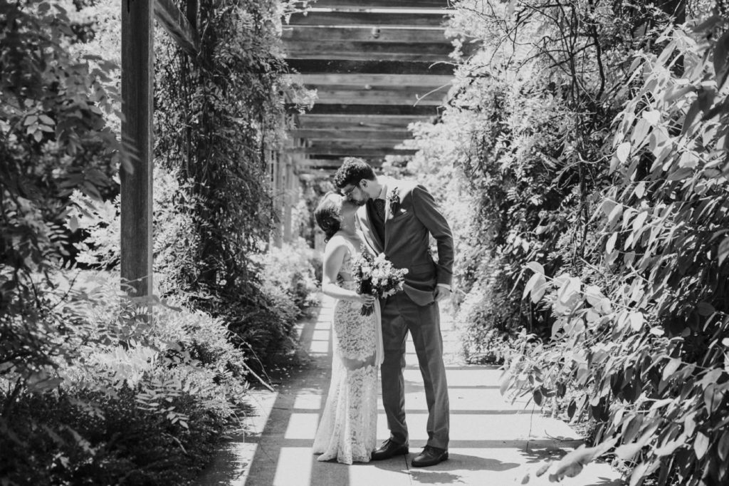 black and white photo of bride and groom surrounded by vines growing over terrace and kissing at Indianapolis Art Center