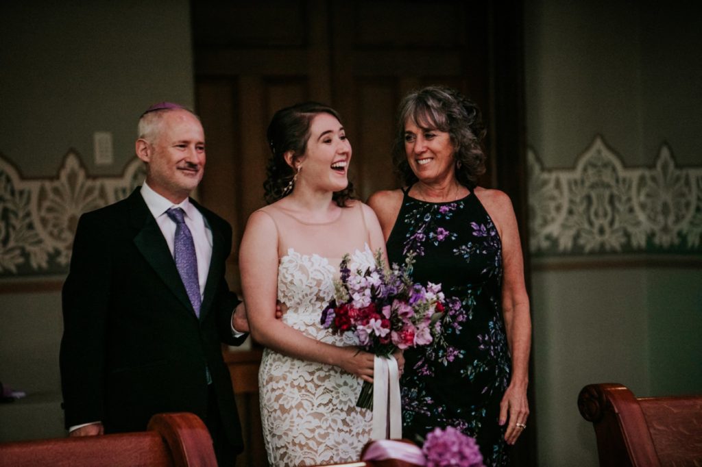 bride walks down aisle with mom and dad in close up shot as they enter their indianapolis venue in the dark
