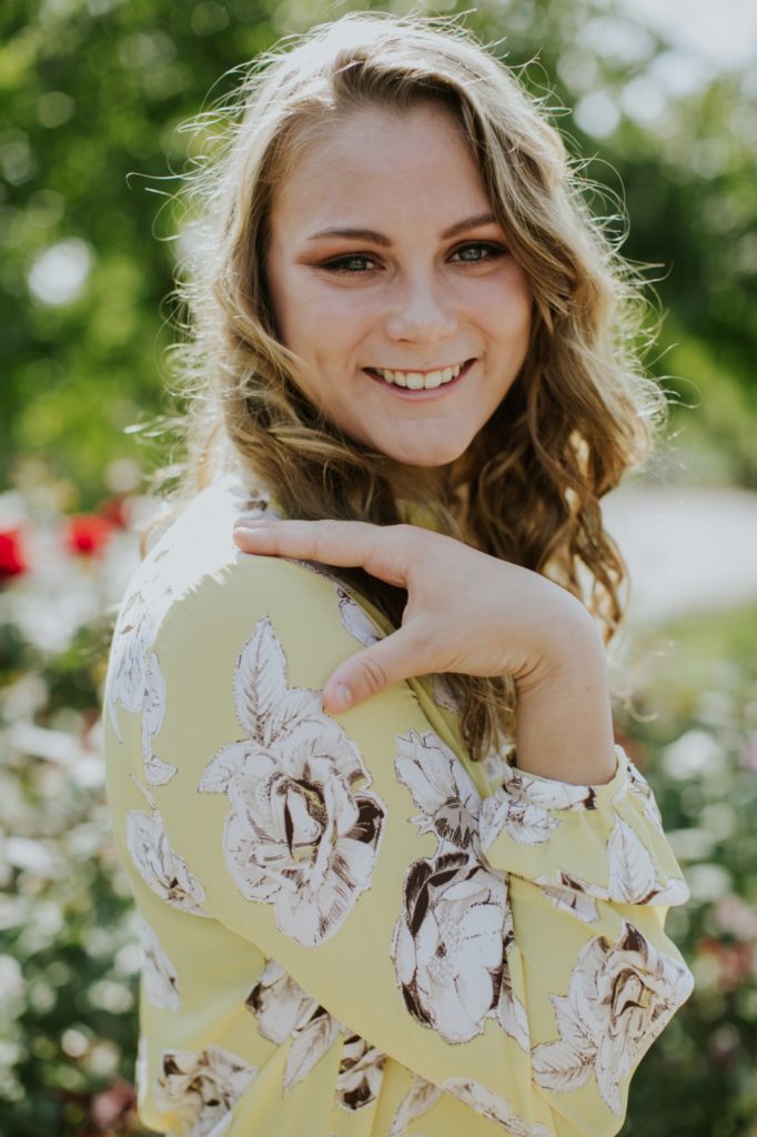 girl in yellow floral dress smiles at camera with hand on her shoulder in this Muncie Indiana Senior Photography