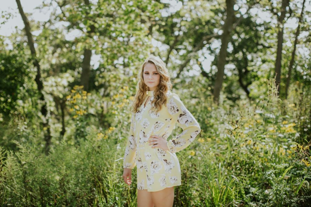 Girl stands in dense forest with hand on hip and smiles in this Muncie Indiana Senior Photography
