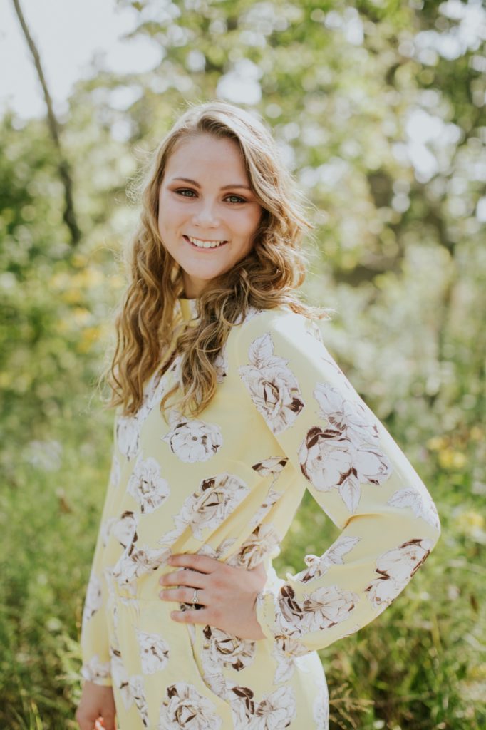 girl in yellow floral dress smiles at camera with hand on hip in this Carmel Senior Portrait