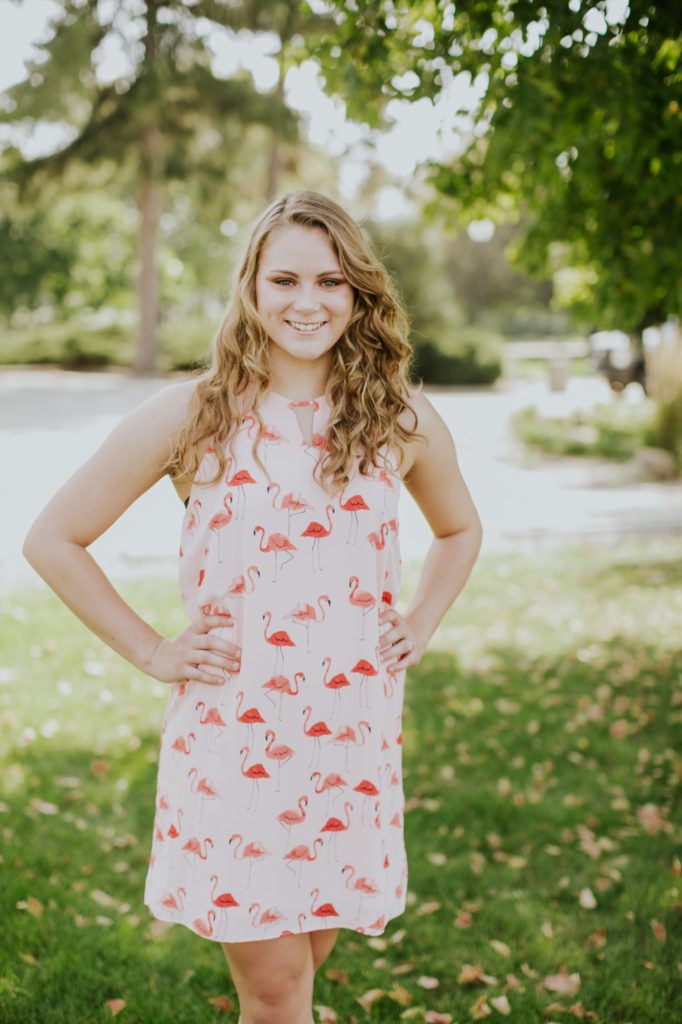 Girl in red dress stands in shade of tree with hands on hips in this Noblesville Senior Portraits