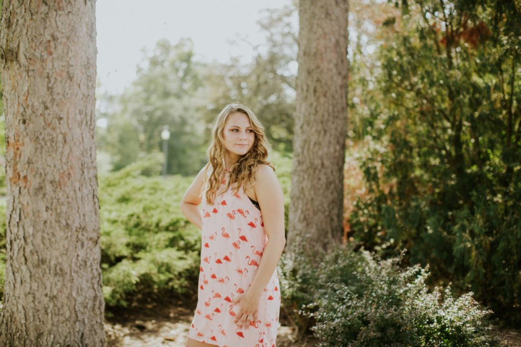 girl in red dress walks amongst the trees at sunset in this Fishers Senior Portraits session