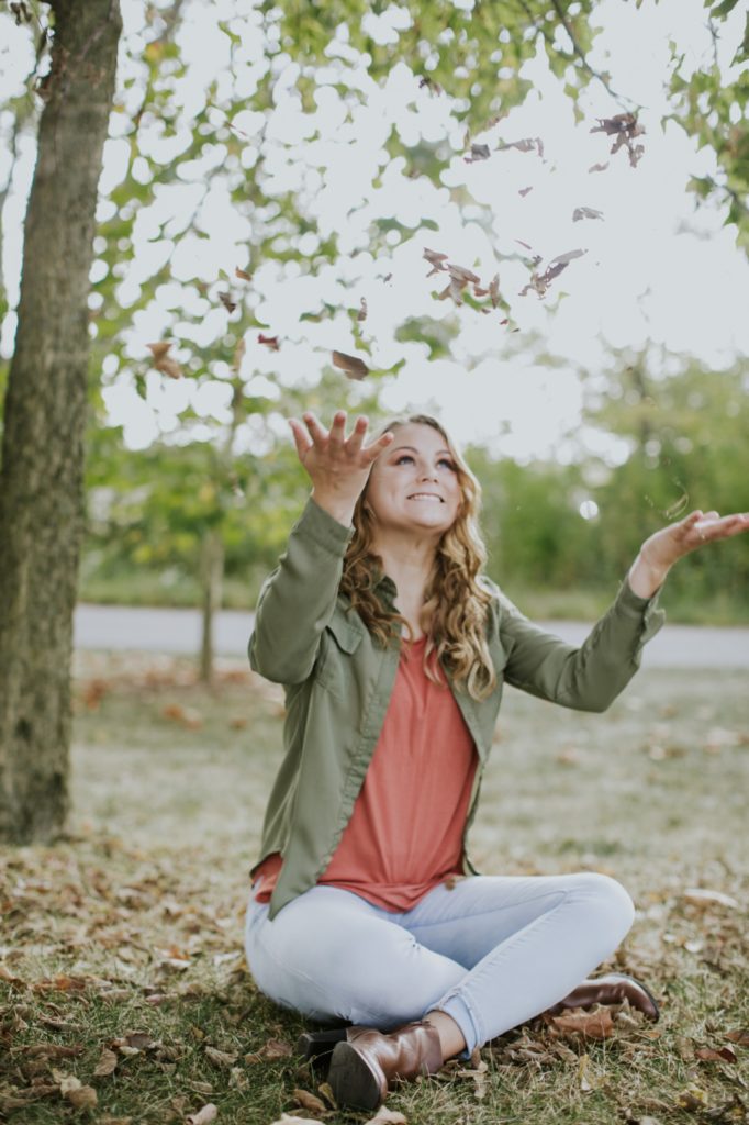blonde girl in orange shirt throws leaves into the air in her Muncie Indiana Senior Portraits