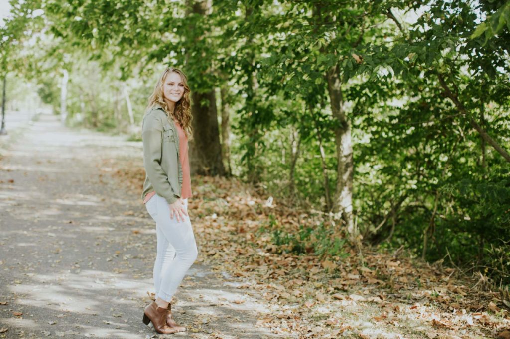girl in jeans and green jacket in woods in Westfield Senior Photo session