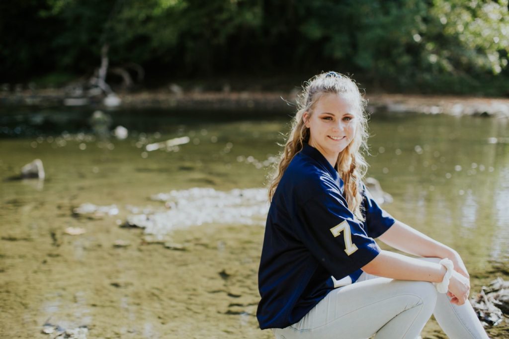 blonde girl in a colts jersey beside a creek in Indianapolis Senior Pictures