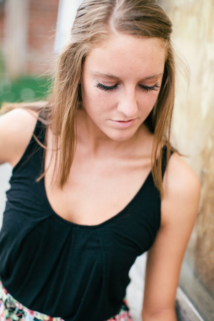 girl in black tank top looks down while leaning against rustic wall in muncie senior photography