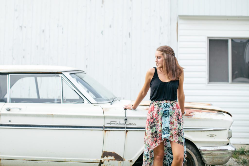 girl in skirt and black tank top leans against old car in muncie senior photography