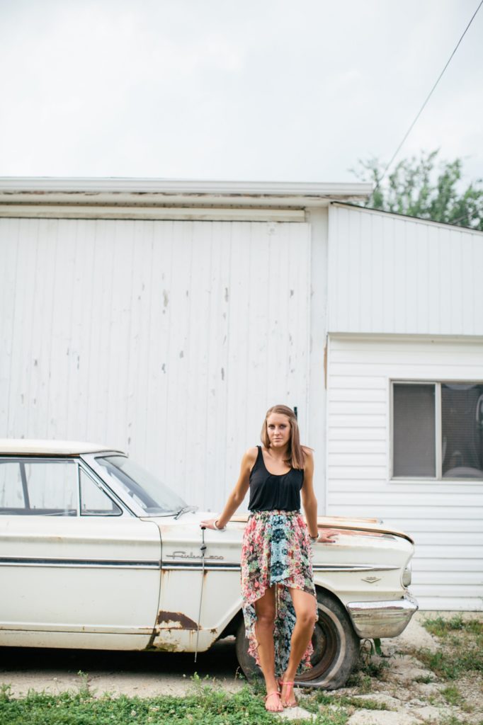 girl in black tank top and skirt leans against antique, rusted car in muncie senior photography