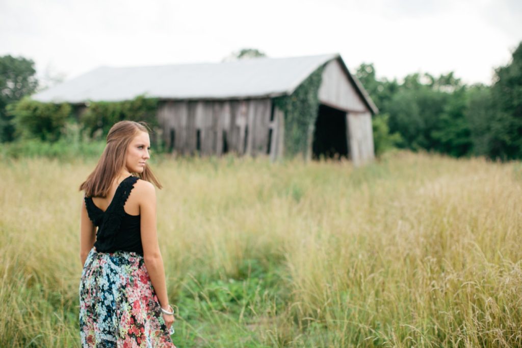 girl in black tank top looks over shoulder in front of dilapidated barn in muncie senior photography