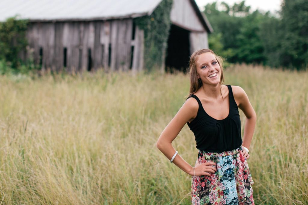 girl laughs in field in front of dilapidated barn in muncie senior photography
