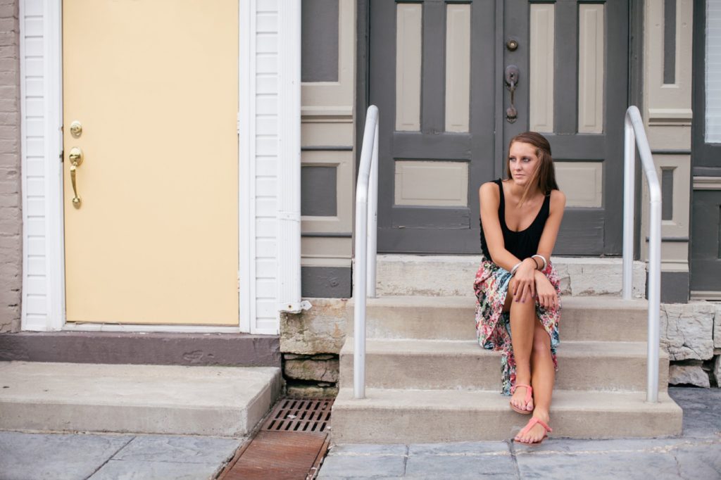 girl in black tank top sits on steps in front of colorful house in muncie senior photography