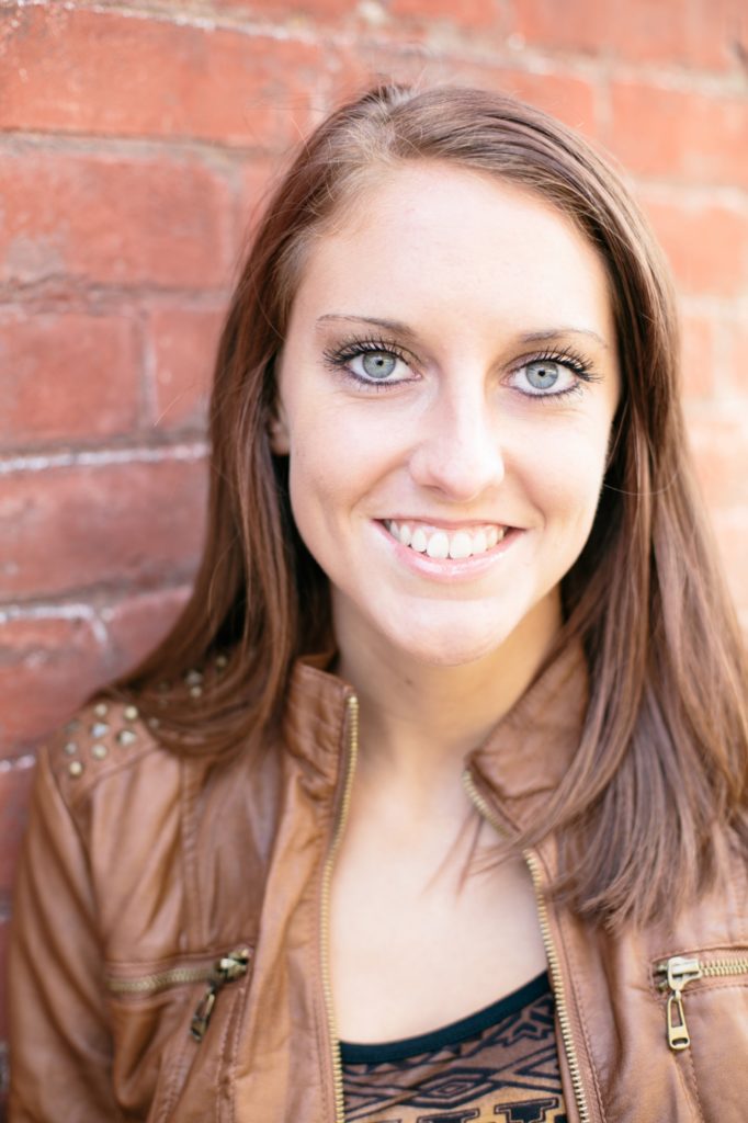 young girl in leather jacket smiles in front of brick in her muncie senior pictures