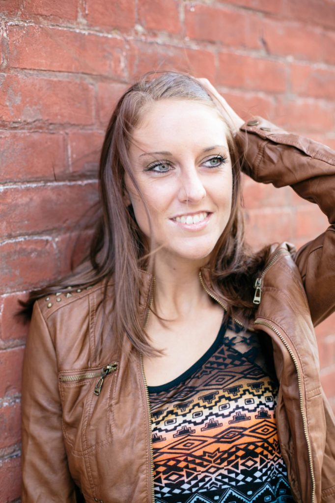 young girl messes with hair in front of brick wall in her muncie senior pictures