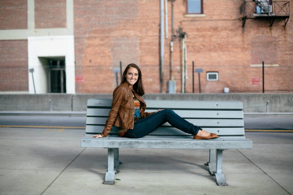 girl in leather jacket sits on bench in muncie senior pictures