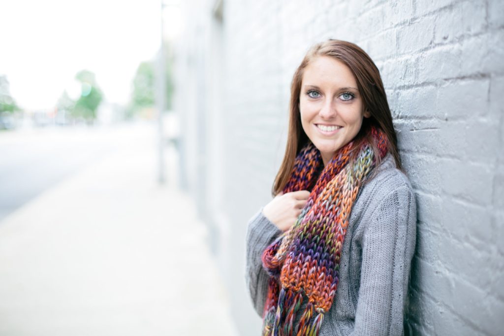 girl in scarf leans against white brick building in Noblesville portraits