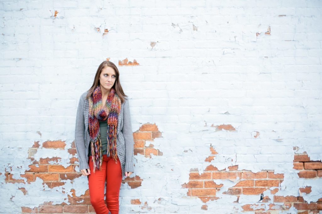 girl in scarf leans against white brick wall with paint that's been worn away in muncie senior pictures
