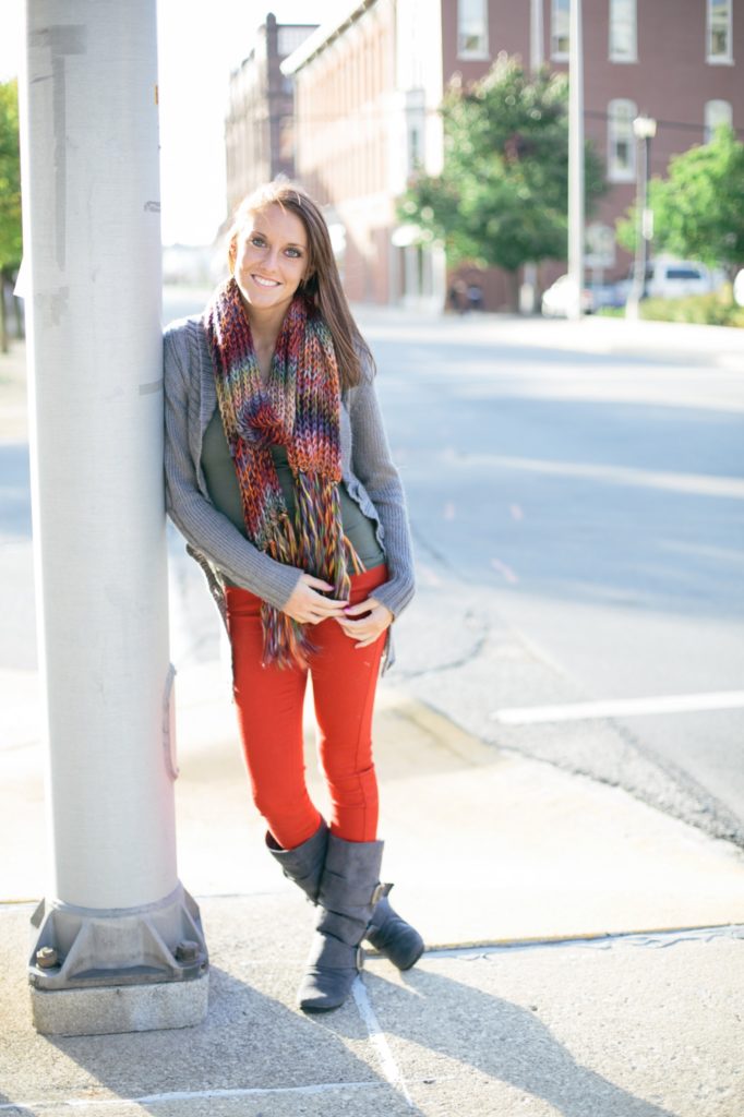 girl in scarf and red pants and boots leans against a telephone pole in muncie senior pictures