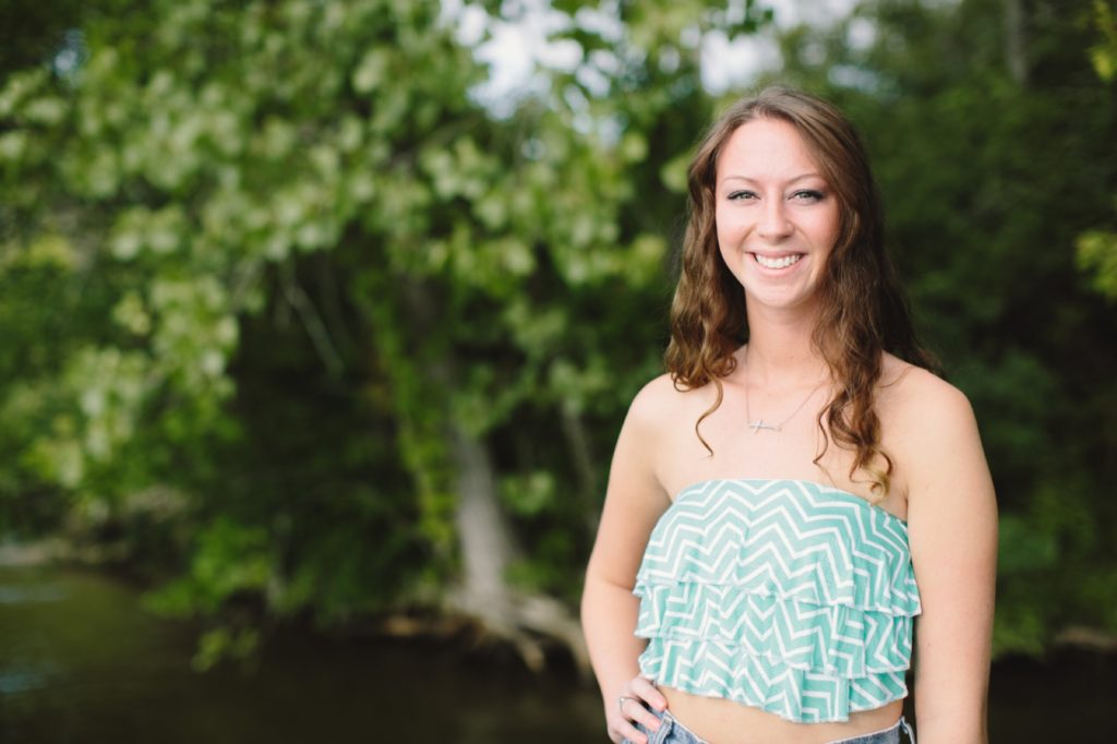 girl with hand on hip stands in front of trees in Muncie senior portraits