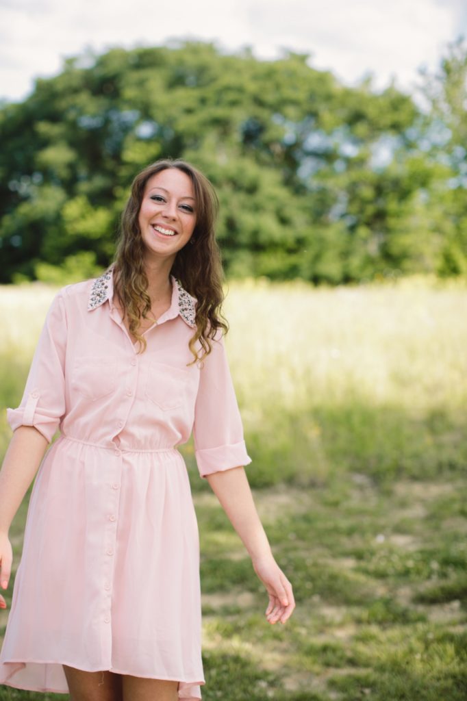 girl in pink dress walks through field of grass in Noblesville Senior Pictures