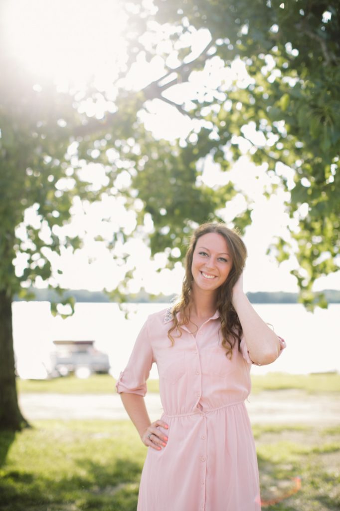 girl in pink dress plays with hair under trees in Fishers senior pictures