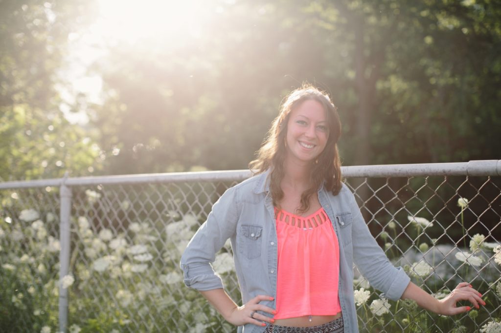 Girl in jean jacket and hot pink top stands in front of fence in Muncie senior portraits